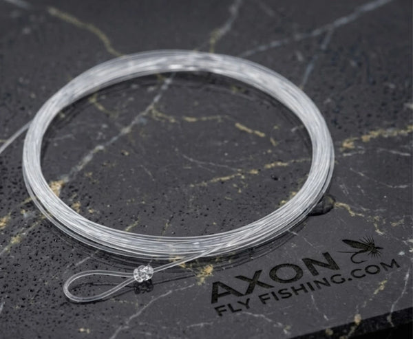 Clear Axon fluorocarbon leader spool, coiled on black marble background with Axon Fly Fishing logo

