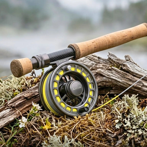 Fly fishing reel in black and aluminum, resting on driftwood in the forest
