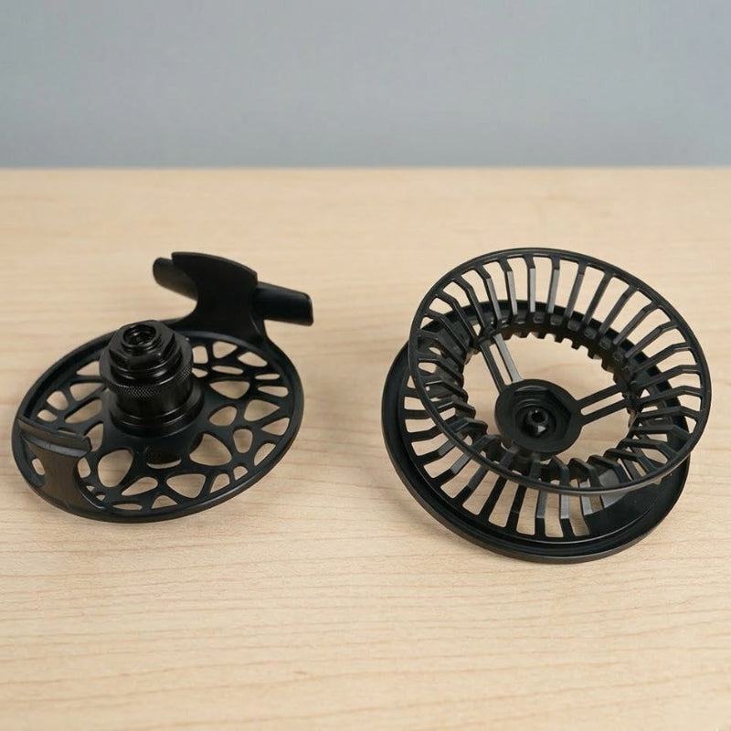 Moulinet de pêche à la mouche moderne Axon avec un cadre noir mat ajouré et une bobine centrale anodisé. sur décors bois
