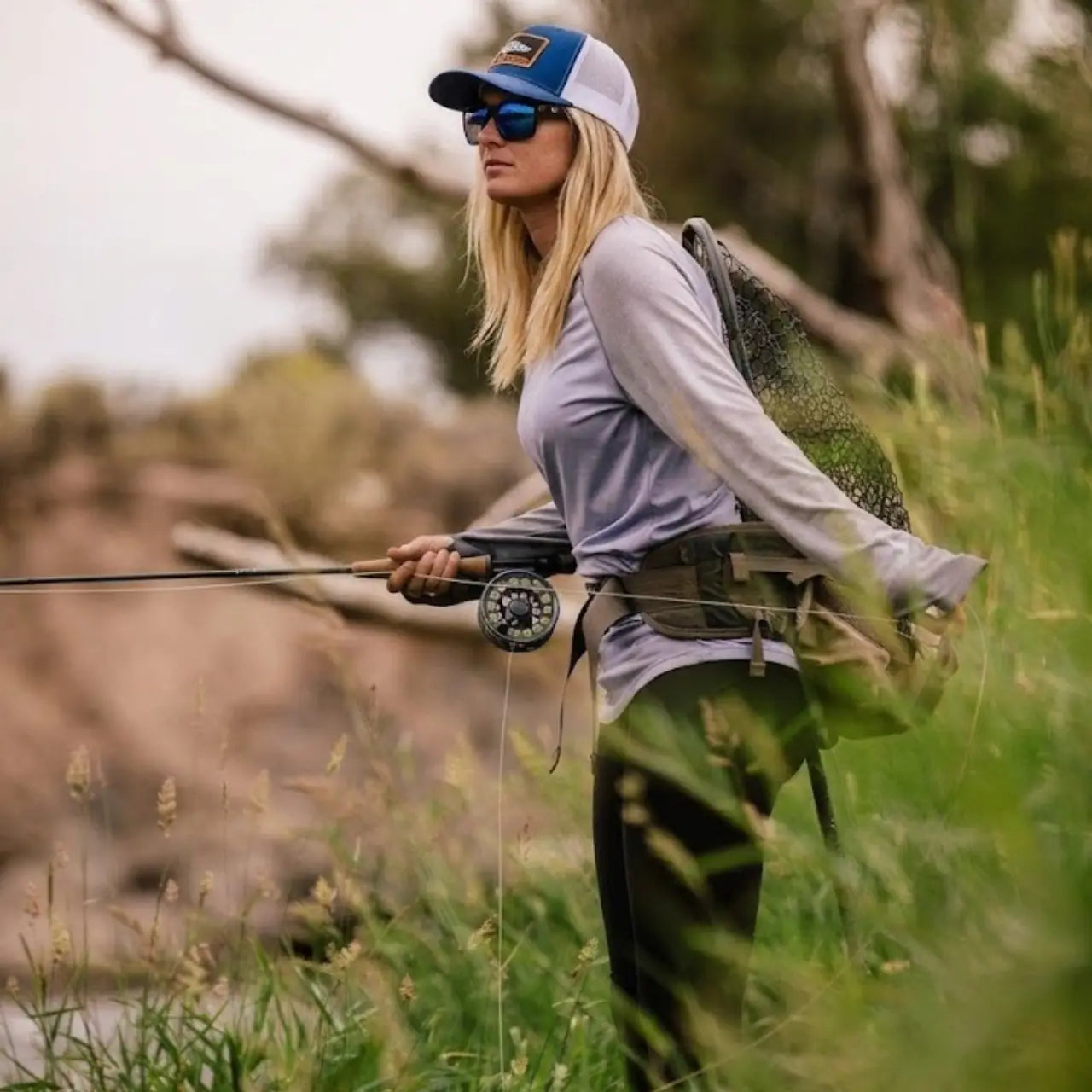 Pêcheuse à la mouche en waders dans une rivière, lancer en cours avec soie formant une boucle